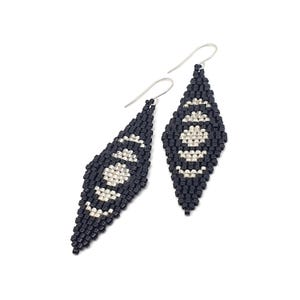 May include: A pair of beaded earrings with a diamond shape. The earrings are primarily black with a silver-colored geometric pattern in the center. The earrings have silver-colored hooks.