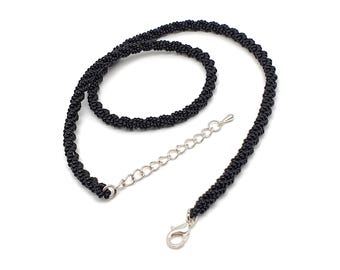 Op de afbeelding: Een zwarte kralenketting met een zilverkleurige sluiting en verlengketting. De ketting is gemaakt van kleine, strak geweven zwarte kralen, waardoor een textuur ontstaat. De sluiting en verlengketting zijn zichtbaar.