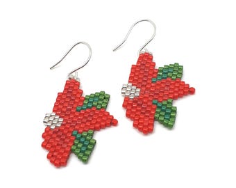 Op de afbeelding: Een paar hangende oorbellen gemaakt van kleine rode, groene en zilveren kralen in een kerstster-bloempatroon. Elke oorbel is voorzien van een zilverkleurige metalen haak voor bevestiging en toont een gedetailleerd, gepixeld bloemmotief.