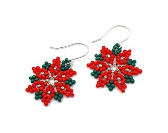 Op de afbeelding: Een paar geborduurde sneeuwvlok oorbellen. De oorbellen zijn rood en groen, met zilverkleurige metalen oorhaken. De oorbellen zijn gemaakt van kleine, ronde kralen gerangschikt in een bloemenpatroon.