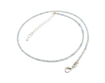 Op de afbeelding: Een delicate ketting met kleine, gefacetteerde lichtblauwe kralen die aan elkaar zijn geregen. Het sieraad is voorzien van een zilverkleurige metalen karabijnsluiting en een verstelbare verlengketting met een kleine ronde bedel.