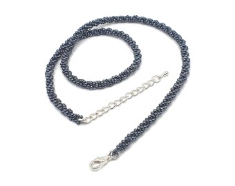 Op de afbeelding: Een donkergrijze kralenketting met een zilverkleurige sluiting en verlengketting. De ketting is gemaakt van kleine, ronde kralen in een gedraaid touwontwerp. De ketting wordt getoond tegen een witte achtergrond.