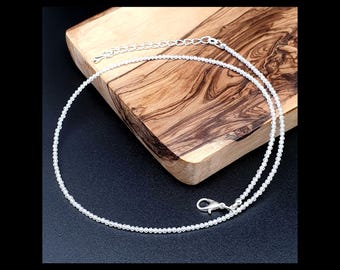 Op de afbeelding: Een zilverkleurige kralenketting bestaande uit kleine, uniforme bolvormige kralen. De ketting is voorzien van een karabijnsluiting en een verstelbare verlengketting met grotere schakels aan het uiteinde voor een pasvorm.