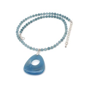 May include: A necklace featuring a strand of small, light blue beads. A silver pendant holds a large, teardrop-shaped, blue pendant with a hole in the center. The necklace has a silver clasp and an adjustable chain.