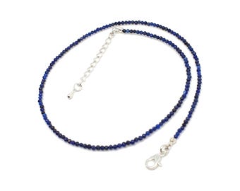 Op de afbeelding: Een verfijnde ketting bestaande uit kleine, gefacetteerde donkerblauwe kralen. Het sieraad is voorzien van een zilverkleurige karabijnsluiting en een verstelbare verlengketting met een kleine druppelvormige bedel.