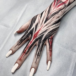 May include: A hand with a black and red abstract tattoo. The tattoo covers the entire hand and part of the forearm. The tattoo is done in a bold, graphic style.