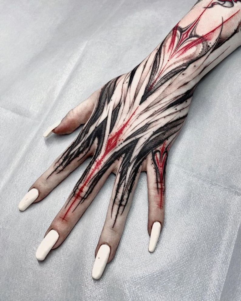 May include: A hand with a black and red abstract tattoo. The tattoo covers the entire hand and part of the forearm. The tattoo is done in a bold, graphic style.