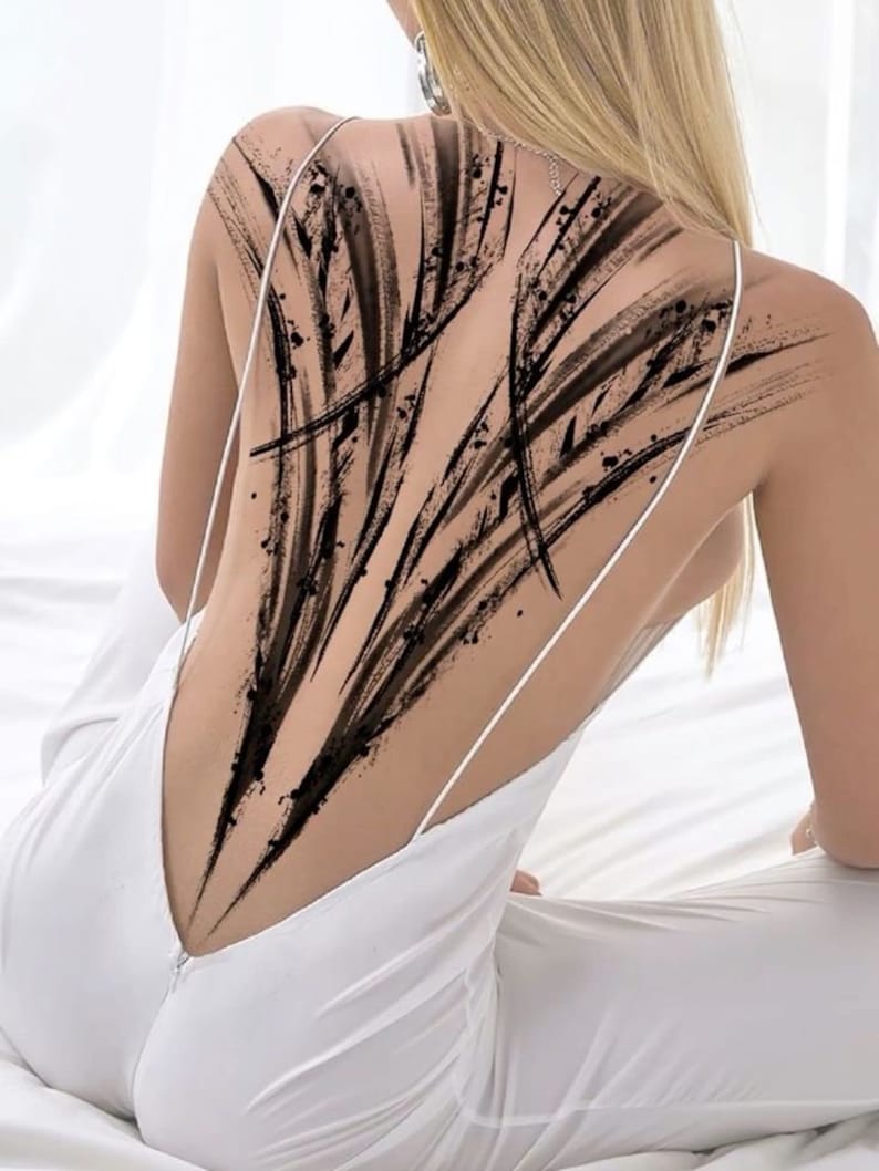 May include: A person with a black abstract tattoo on their back. The tattoo is made up of a series of lines and shapes that create a dynamic and eye-catching design.