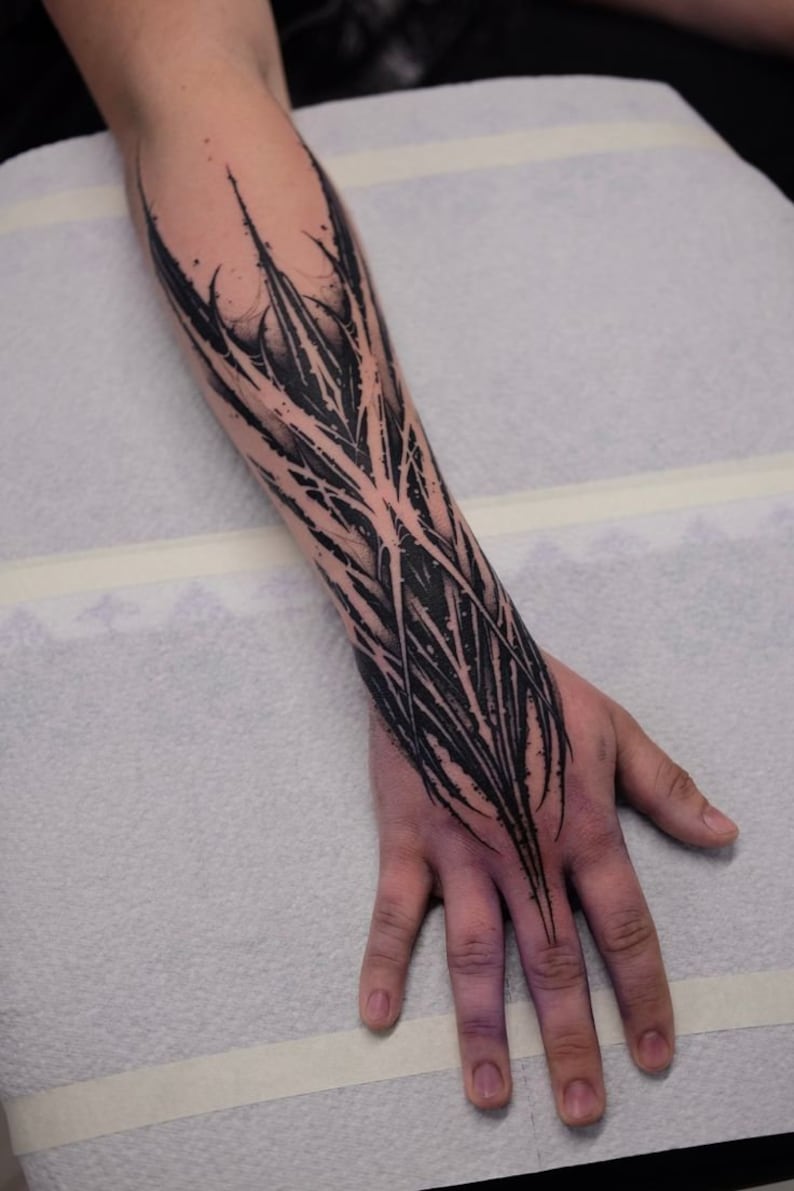 May include: A black and white abstract tattoo design on a person's forearm and hand. The design features sharp, jagged lines and shapes.