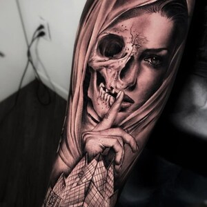 May include: Black and white tattoo design of a woman's face with a skull overlay. The woman's face is partially obscured by a hood, and she is holding her finger to her lips in a gesture of silence. The tattoo is on a person's arm.
