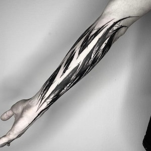 May include: Black and white abstract tattoo design on a person's forearm. The design features sharp, jagged lines and shapes that create a sense of movement and energy.