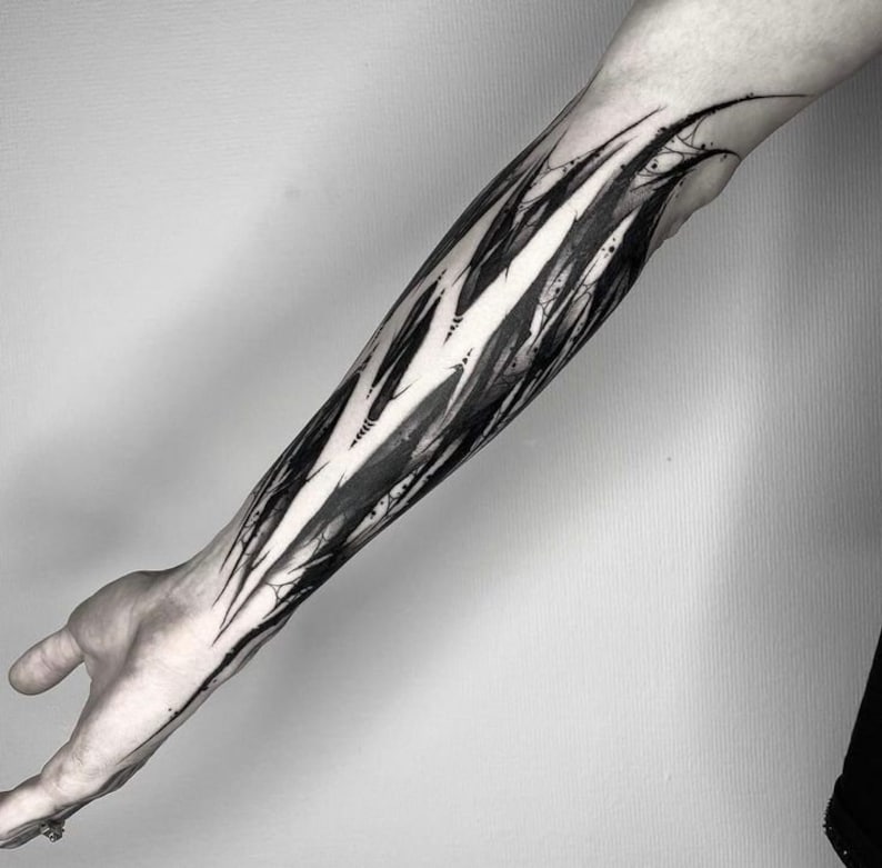 May include: Black and white abstract tattoo design on a person's forearm. The design features sharp, jagged lines and shapes that create a sense of movement and energy.