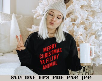 Könnte beinhalten: Ein schwarzer Pullover mit dem Text "Merry Christmas Ya Filthy Animal" in roten Buchstaben. Die Person, die den Pullover trägt, hält eine weiße Tasse mit einem braunen Henkel.
