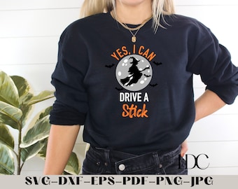 May include: A black sweatshirt with a white circle and a witch flying on a broomstick. The text "YES, I CAN DRIVE A STICK" is printed in orange on the sweatshirt.