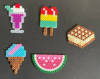 May include: A collection of colorful, pixelated food items made from plastic beads. The items include a sundae, popsicle, ice cream cone, ice cream sandwich, and a watermelon slice. The sundae has a cherry on top, and the ice cream cone is blue and pink.