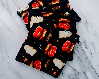 Puede incluir: Cuatro cuadrados de tela negra con temática de Halloween. Cada cuadrado presenta un fantasma blanco, tazas de mantequilla de cacahuete Reese's naranja y roja y una estrella negra. La tela es negra con fondo blanco.