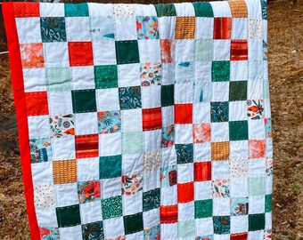 May include: A patchwork quilt with a red border and a checkerboard pattern of white, green, and red squares. Each square features a different floral print.