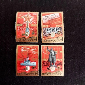 May include: Four rectangular postage stamps from the USSR, each featuring a red and gold color scheme, the years 1917 and 1977, and the text POCHTA SSSR. The designs include a star, a document, a ship, and a statue of a figure in a suit.