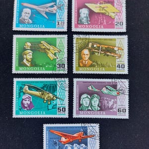 Pode incluir: Uma coleção de sete selos postais retangulares da Mongólia, cada um apresentando uma aeronave histórica diferente e o retrato de um piloto ou inventor. Os selos são impressos em várias cores, incluindo azul, rosa, verde, amarelo e roxo.