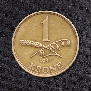 Peut inclure: Une pièce de monnaie circulaire de couleur laiton présentant le chiffre 1 au centre, au-dessus d'un épi de blé et d'une tige d'avoine horizontaux. L'année 1947 est inscrite sous les céréales, avec le mot KRONE courbé le long du bord inférieur.