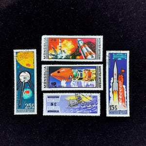 May include: A collection of five rectangular postage stamps from Mongolia featuring space exploration themes. The stamps display illustrations of rockets, satellites, and launch pads with text including Mongolia, 20, 10, 25, 5, and 15.