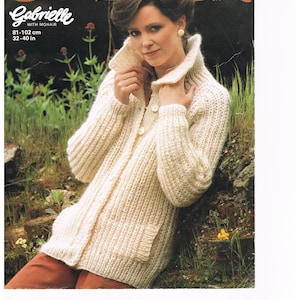 May include: A white knitted cardigan with a button closure and a collar. The cardigan is made with mohair and has a relaxed fit. The model is wearing the cardigan with a pair of brown pants. The text "Gabrielle with mohair 81-102 cm 32-40 in" is printed on the image.