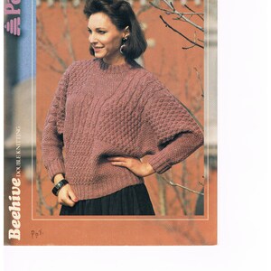 Könnte beinhalten: Eine Frau trägt einen mauvefarbenen Strickpullover mit strukturiertem Muster. Der Pullover hat einen Rundhalsausschnitt und lange Ärmel. Das Bild enthält den Text "Patons" und "Beehive Double Knitting". Die Größe des Pullovers ist 81-97 cm.