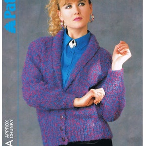 May include: A blue and purple cardigan with a shawl collar and button closure. The cardigan is made with a chunky yarn and has a textured knit. The model is wearing a blue shirt underneath the cardigan.