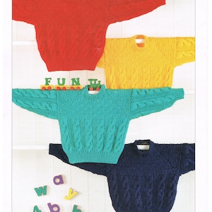 May include: Image of four Aran-style knit sweaters in red, yellow, teal, and navy blue. The sweaters are displayed on a white background. The word "FUN" is spelled out with wooden letters and a toy train is placed on top of the teal sweater. The text "SNUGGLY ARAN" and "SIRDAR" are also visible.