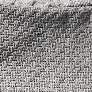 Könnte beinhalten: Nahaufnahme einer grauen Strickdecke mit einem strukturierten Webmuster. Die Decke hat ein Flechtmuster mit einem Rand aus einem anderen Strickmuster. Die Decke ist aus einem weichen, bequemen Material gefertigt.