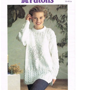 May include: A white knitted sweater with a cable knit pattern and a diamond-shaped design in the center. The sweater has a crew neck and long sleeves. The sweater is featured in Patons Laguna DK yarn. PBN C 4961 30-40 in.