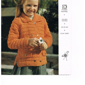 May include: A young girl wearing an orange knitted cardigan with buttons. The cardigan has a collar and pockets. The girl is holding a white flower.