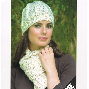 Könnte beinhalten: Ein weißes Strickmützen- und Schals-Set mit einem Zopfmuster. Die Mütze hat eine lockere Passform und der Schal ist lang und breit. Das Set wird an einem Modell mit braunen Haaren und einem braunen Shirt gezeigt. Das Bild enthält den Text "Tivoli 3587" und "KNITS TO ARAN".