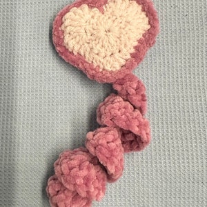 May include: A pink and white crocheted heart-shaped toy with a long, pink, crocheted tail.