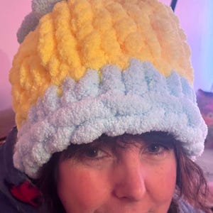 Puede incluir: Un gorro de crochet amarillo y azul claro. El gorro está hecho con un hilo esponjoso y tiene un diseño texturizado.