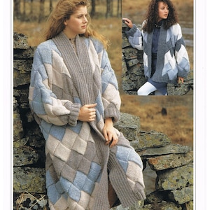 May include: A long, chunky knit cardigan with a diamond pattern in shades of blue, beige, and brown. The cardigan is open in the front and has a long, flowing shape. The model is wearing the cardigan over a white shirt and white pants. The cardigan is shown against a backdrop of a stone wall.