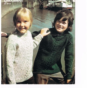 May include: A vintage knitting pattern featuring two children wearing jumpers. The girl is wearing a white jumper with a green pattern and the boy is wearing a green jumper with a white pattern. The pattern is titled "Buccaneer" and is for sizes 26-34 inches.