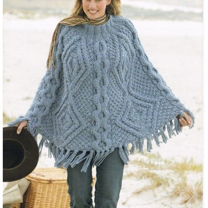 Puede incluir: Un poncho azul de punto con un patrón de trenza y ribete de flecos. El poncho es de talla única y está hecho por Sirdar.