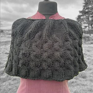 May include: A black knitted shawl with a textured pattern. The shawl is draped over a mannequin wearing a pink dress.