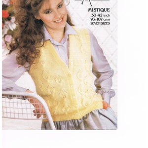 May include: A woman wearing a yellow knitted vest with a leaf pattern. The vest has a button-up front and is worn over a light purple collared shirt. The text "MISTIQUE" and size information (30-42 inch, 76-107 cms) are visible.