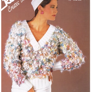 May include: A white sweater with a v-neck and a button closure. The sweater has a textured, fuzzy look and is covered in small, colorful pom-poms. The sweater is being modeled by a person wearing a white hat and white pants. The text "CHARADE 30 - 40 inch 76 - 102 cm" is visible in the upper right corner of the image.