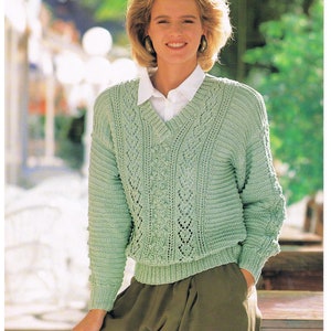 May include: A light green knitted sweater with a V-neck and a cable knit pattern. The sweater is worn by a person with short blonde hair and is paired with a white collared shirt and brown pants. The image includes the text "1452A DOUBLE KNITTING 71-107 cm 28-42 in. Four sizes".