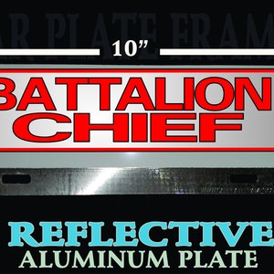 May include: A reflective aluminum car license plate frame with the text "Battalion Chief" in red letters on a white background. The frame measures 10 inches wide and 4 inches tall.