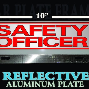 May include: A reflective aluminum car license plate frame with the text "SAFETY OFFICER" in red letters on a silver background. The frame measures 10 inches wide by 4 inches tall.