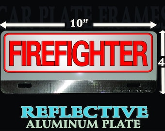 May include: A silver reflective car license plate frame with the word "FIREFIGHTER" in red letters. The frame measures 10 inches wide and 4 inches tall. It is made of aluminum and is designed to be used on a car license plate.