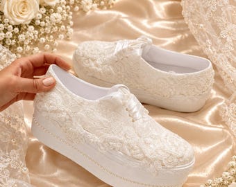 May include: A pair of white platform sneakers featuring intricate floral lace overlays, satin ribbon laces, and a delicate row of small white pearls embedded along the base of the thick rubber soles.