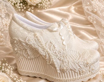 May include: A pair of ivory wedge shoes featuring white lace overlays, floral embroidery, and small pearl embellishments. The shoes have satin ribbon laces and a vertically ribbed wedge heel base, accented with a delicate row of pearls along the sole.