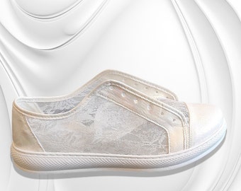 Könnte beinhalten: Ein weißer Sneaker mit einem zarten Spitzenüberzug an den Seitenteilen, einer soliden weißen Zehenkappe und einer strukturierten weißen Gummisohle. Der Schuh hat eine flache Silhouette mit einem verstärkten Ösenstreifen und einer glatten Fersenkappe.