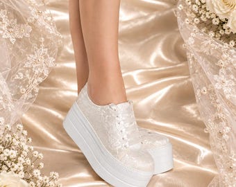 Könnte beinhalten: Ein weißer, mit Spitze überzogener Plateau-Sneaker mit einer dicken, massiven weißen Gummisohle und passenden weißen Satin-Schnürsenkeln. Der Schuh hat eine abgerundete Zehenpartie und eine flache Silhouette, wobei sich das florale Spitzenmuster über das gesamte Obermaterial erstreckt.
