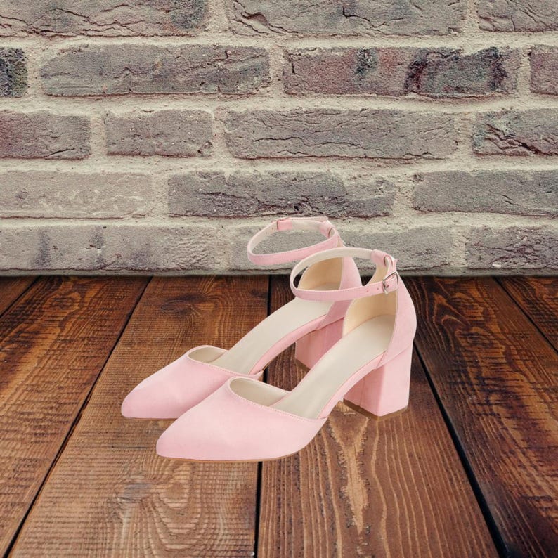 May include: A pair of light pink suede heeled shoes with ankle straps. The shoes have a pointed toe and a block heel.